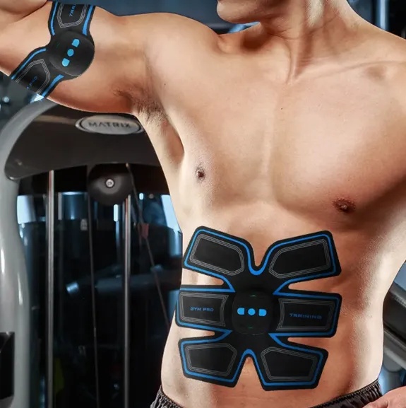 Fitness enthusiast using EMS Abs Stimulator as a training enhancement tool in a modern gym environment alongside traditional workout equipment